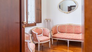 A room with a wooden floor, a white wall, a round mirror, and two pink upholstered chairs with gold trim. - Siracusa Horizon Home by Wonderful Italy (Siracusa)