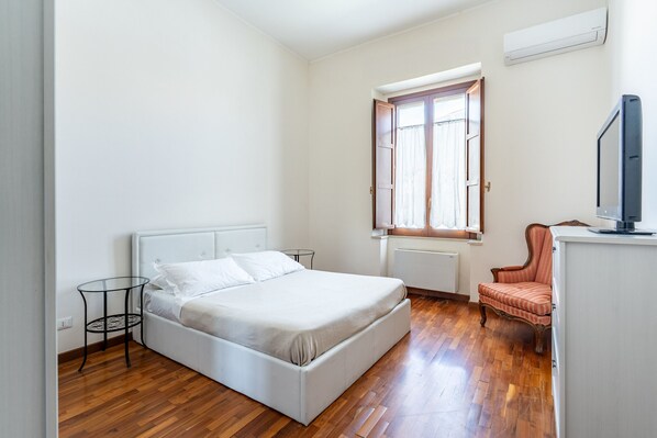 A bedroom with a bed, a small table, a chair, a TV, and a window with curtains. - Siracusa Horizon Home by Wonderful Italy (Siracusa)