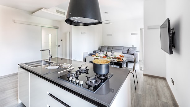 Una cocina moderna con una isla central, un área de comedor con un sofá gris y un televisor de pantalla plana montado en la pared.