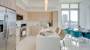 A modern kitchen with a central island, stainless steel appliances, and a dining area with blue chairs and a white table. - DESIGN DISTRICT LUXURY 2/2 PARADISE Q602 (Miami)