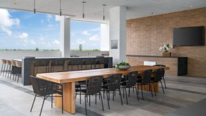 A modern outdoor dining area with a long wooden table and black chairs, a brick wall, and a large TV mounted on the wall. - DESIGN DISTRICT LUXURY 2/2 PARADISE Q602 (Miami)