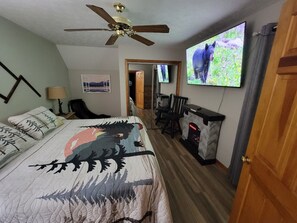 Ein Schlafzimmer mit einem Bett, Deckenventilator, Kamin, Fernseher und einer Tür.