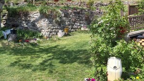 Un mur de pierres avec un petit nichoir, une clôture en bois et un espace jardin agrémenté de diverses plantes et fleurs.