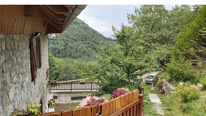Un bâtiment en pierre doté d’un balcon en bois qui donne sur un jardin et une montagne.