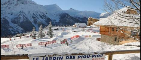 A snowy mountain landscape with a sign reading "LE JARDIN DES PIOU-PIOU de 3 à 6 ans".