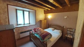 Um quarto pequeno e aconchegante com uma cama de solteiro, uma janela com cortinas, um guarda-roupa de madeira e uma cadeira.