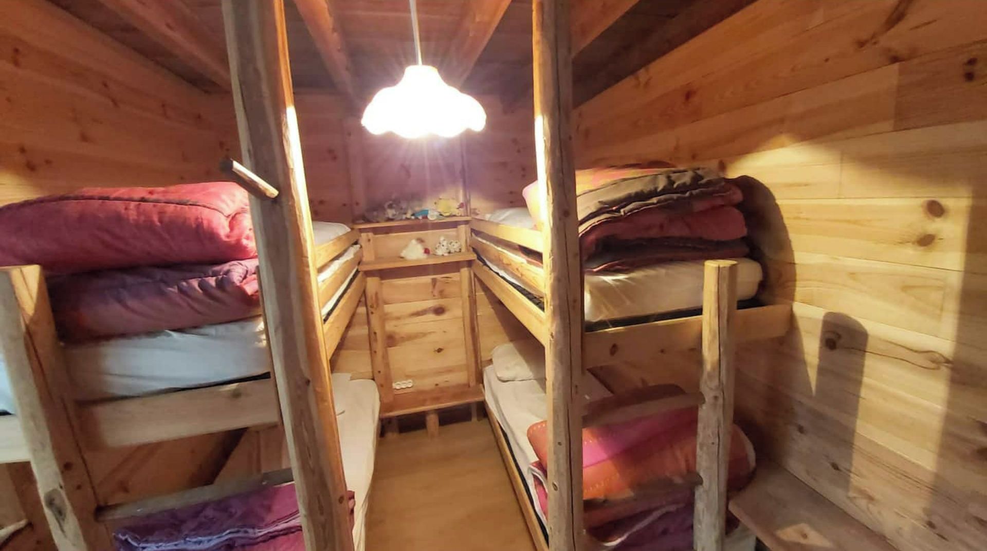 En træhytte med køjesenge, et lille skrivebord og en hængende lampe.
