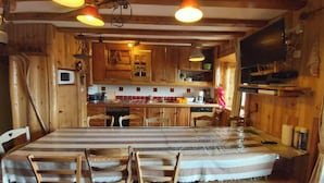 Un intérieur rustique en bois, avec une table à manger, des chaises et un coin cuisine doté de meubles en bois et d’un téléviseur.