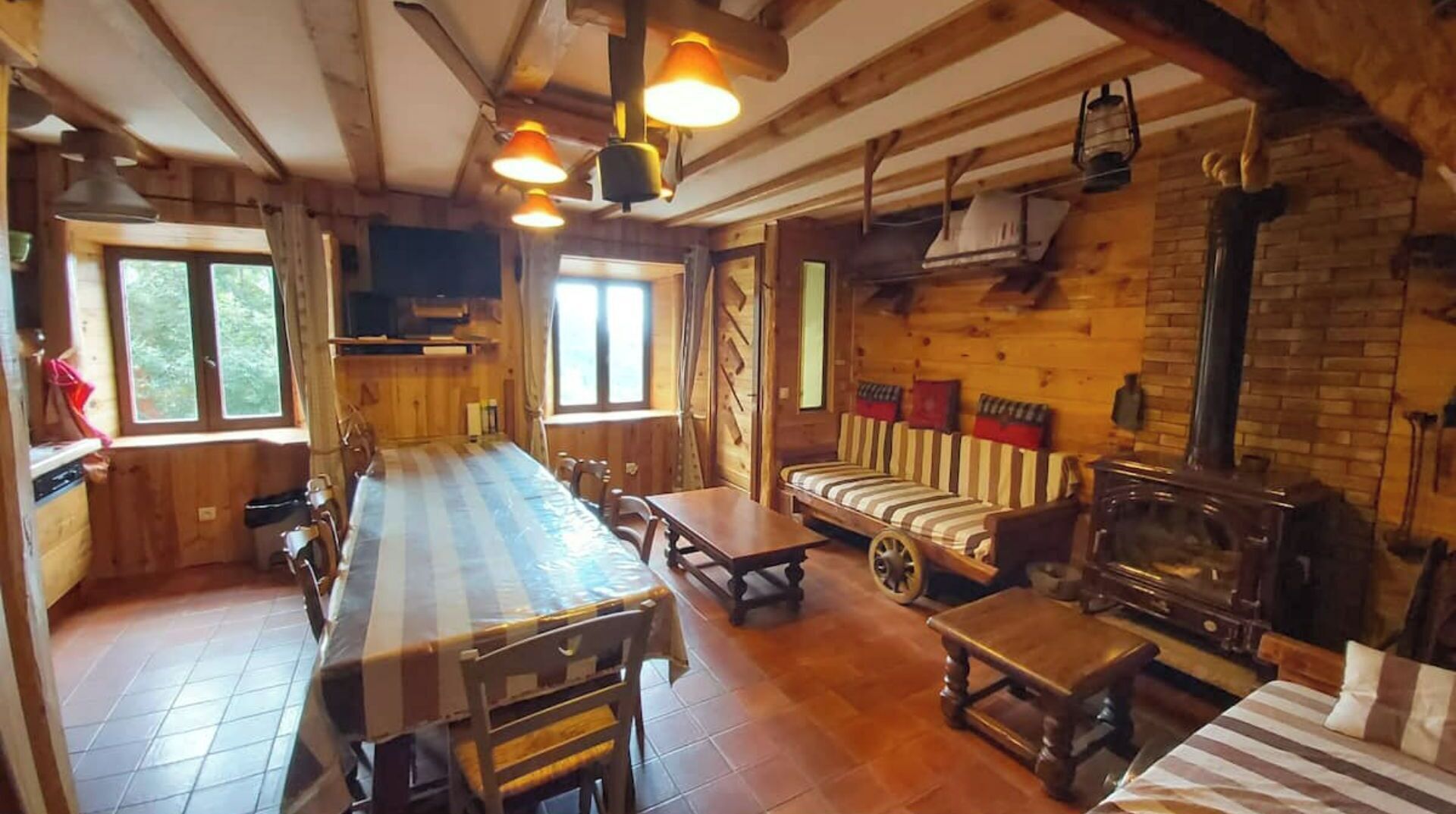 Een gezellig interieur van een blokhut, met een lange eettafel, een bank en een houtkachel.