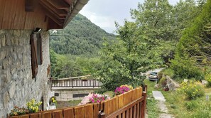 Un bâtiment en pierre doté d’un balcon en bois qui donne sur un jardin et une montagne.