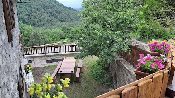 Une terrasse en bois avec une table et des bancs, entourée d’un mur de pierre et d’une clôture en bois.