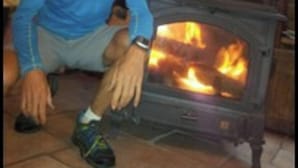 Une personne assise devant un poêle à bois dans une cabane en rondins.