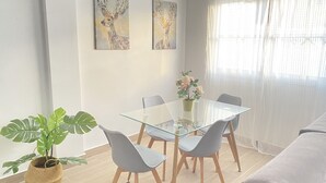 A modern living room with a glass dining table, grey chairs, a sofa, and a potted plant. - HomeForGuest Two bedroom Apartment with pool and terrace (Antigua - Fuerteventura)