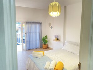 A hotel room with a bed, a potted plant, a bedside table with a lamp, and a view of the outside. - Apartamento Sunny Terrace (Antigua - Fuerteventura)