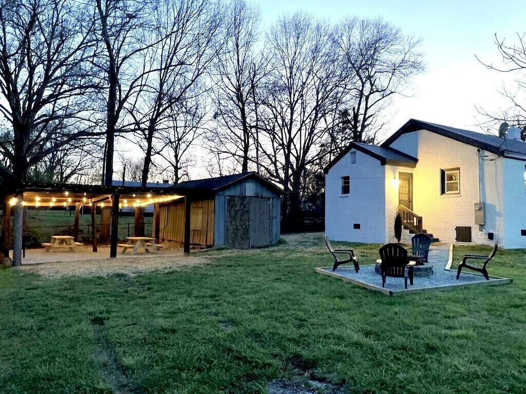 A backyard with a covered patio area, picnic tables, and a white house with a visible garage.