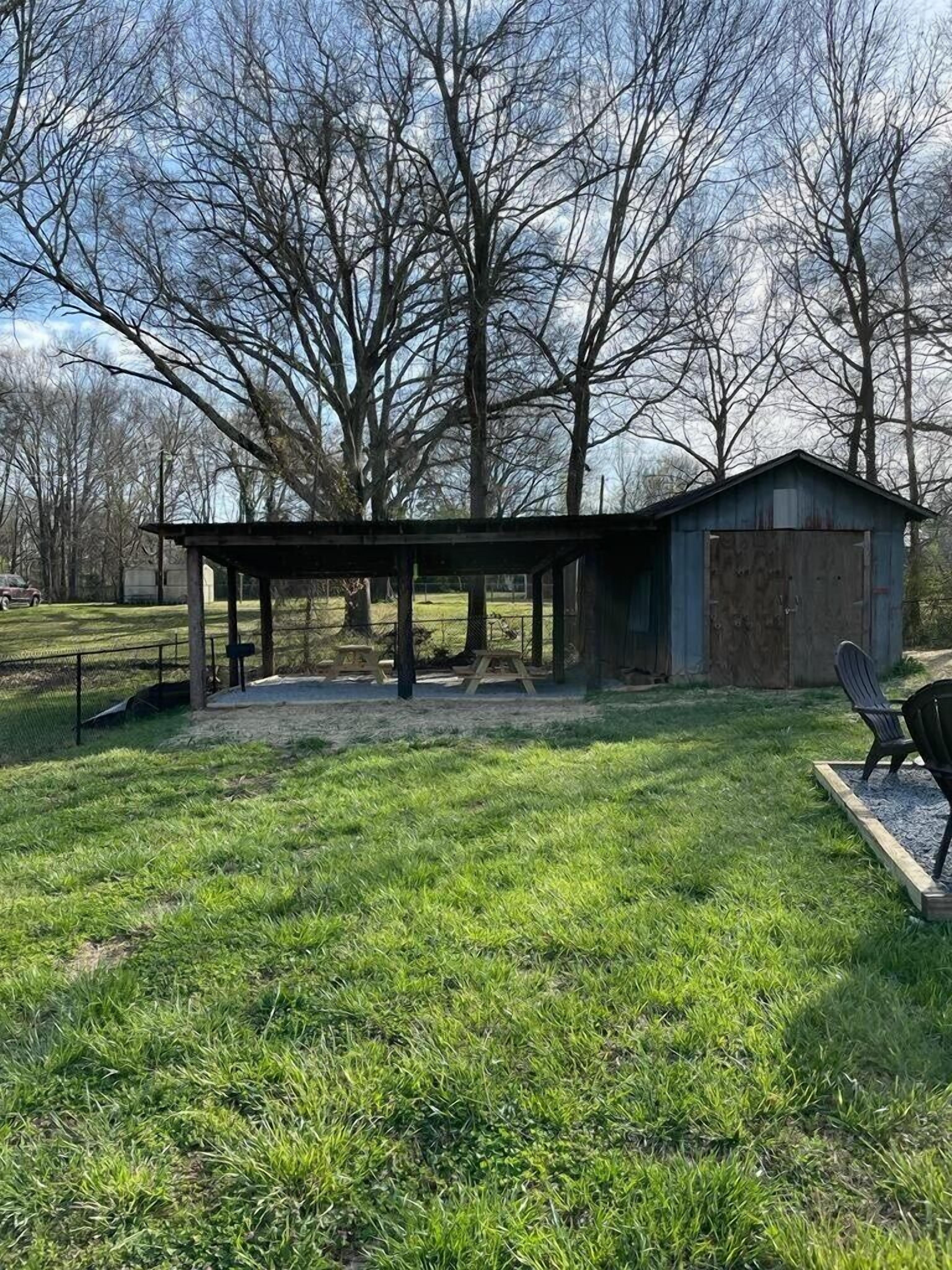 A rustic outdoor area with a wooden pavilion, picnic tables, and a shed.