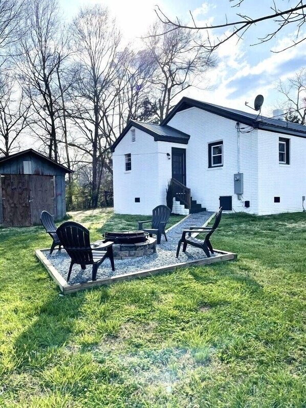 A white house with a fire pit and outdoor seating.