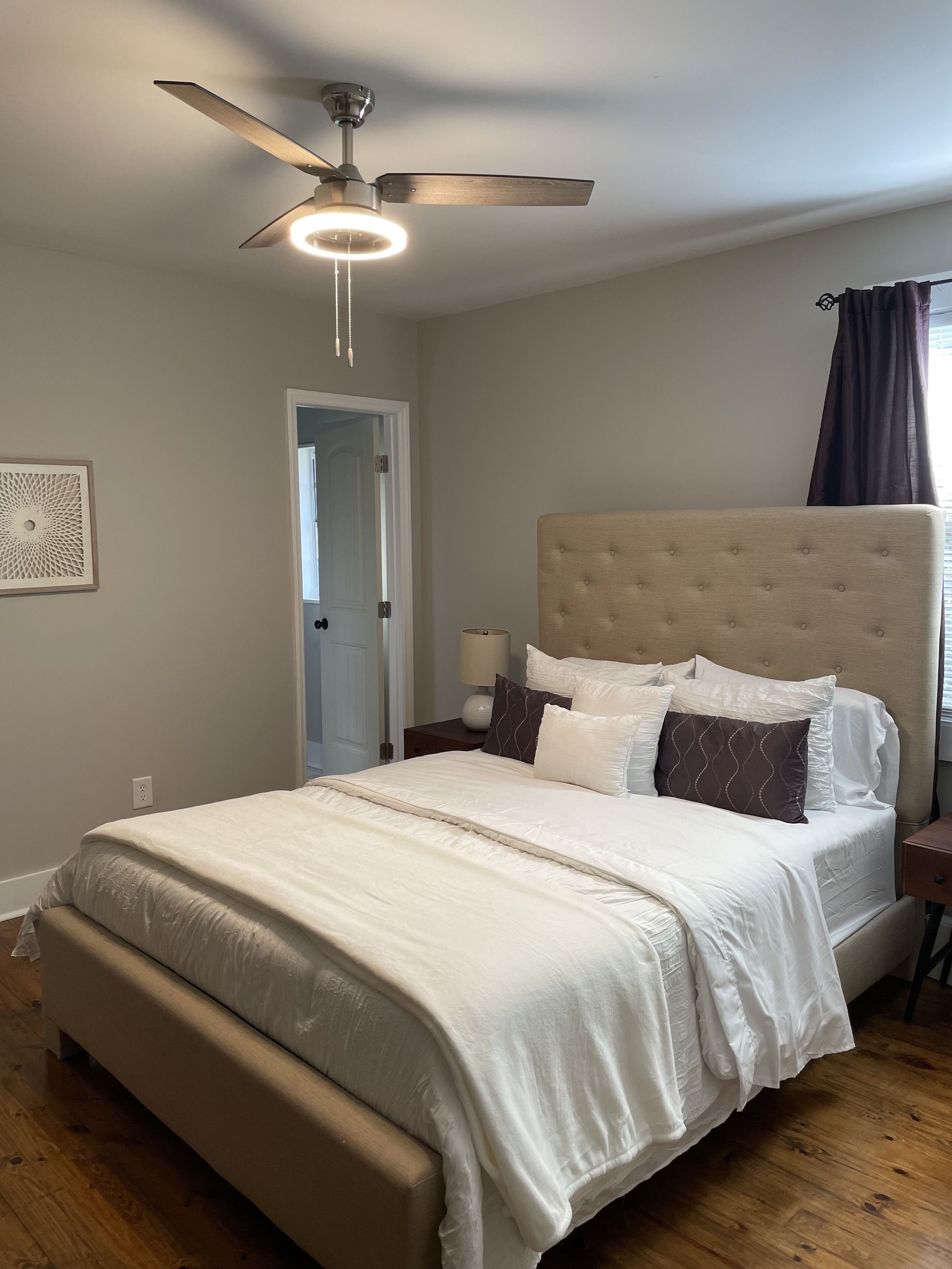 Un dormitorio con cama, ventilador de techo, mesita de noche y lámpara de pared.