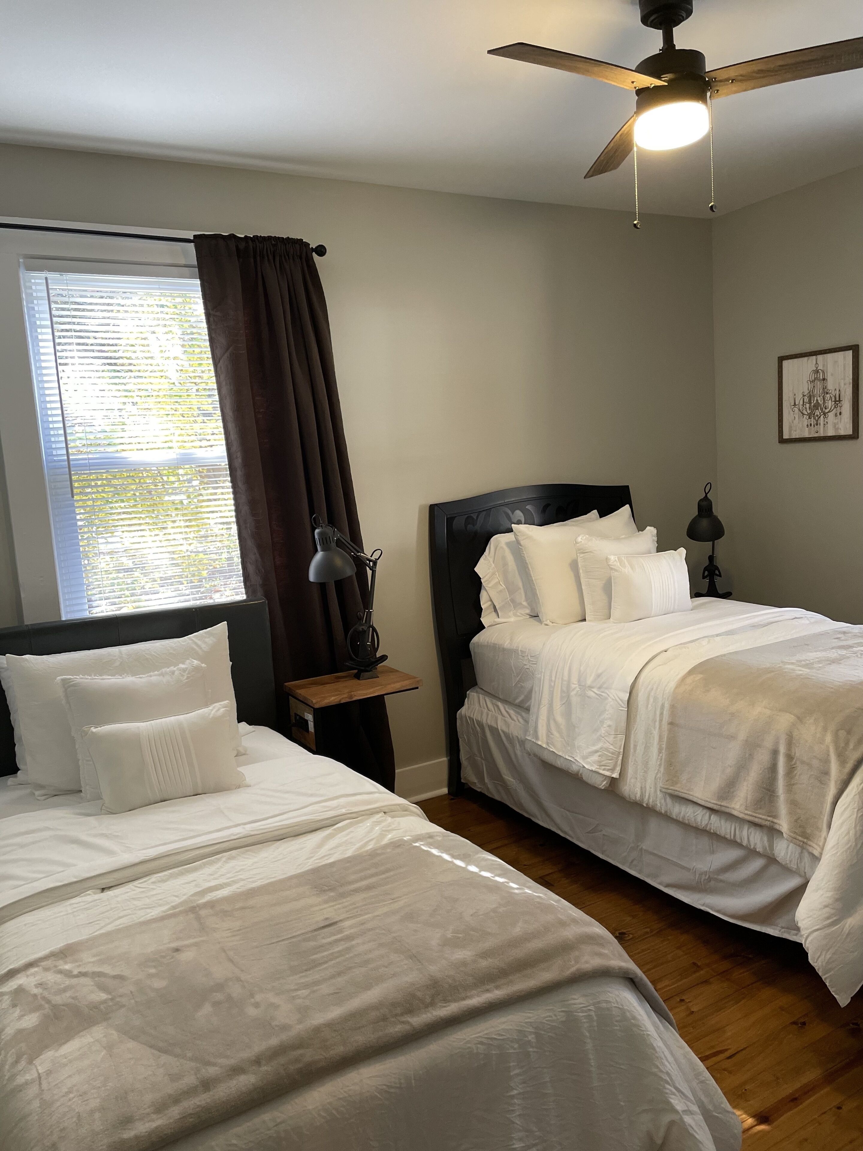 A bedroom with two beds, a ceiling fan, a nightstand with a lamp, and a window with curtains.