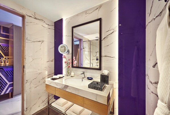 Une salle de bain moderne avec un lavabo en marbre, un grand miroir et un mur d’accent de couleur violette.