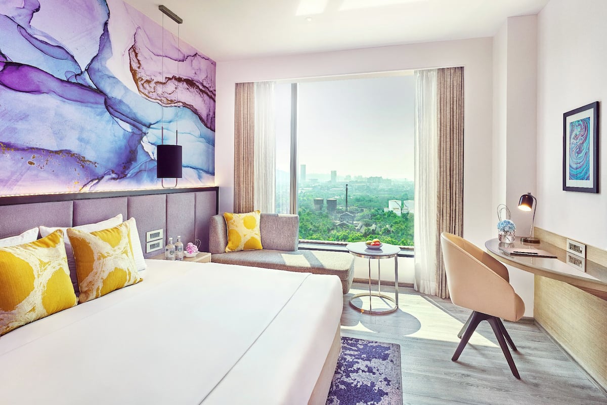 Una habitació d'hotel moderna amb un llit gran, una taula de treball i vistes a la ciutat.