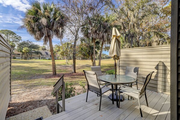 A patio with a round table and four chairs, surrounded by a wooden deck and a fence.
