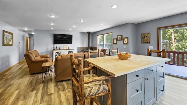 Un vaste espace de vie doté d’un plancher en bois, d’un grand îlot central avec un dessus en bois et d’une table à manger avec des chaises.