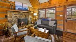 A log cabin interior with a stone fireplace, a sofa, and a coffee table. - Rave ReVIEWs! HOA Pool! Fire Pit! Hot Tub! Arcade! (Gatlinburg)