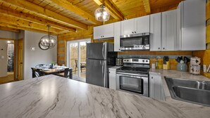 A modern kitchen with marble countertops, stainless steel appliances, and wooden ceiling beams. - Rave ReVIEWs! HOA Pool! Fire Pit! Hot Tub! Arcade! (Gatlinburg)