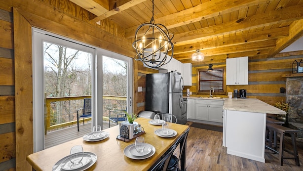 A wooden cabin with a dining area, kitchen, and a large window overlooking a deck. - Rave ReVIEWs! HOA Pool! Fire Pit! Hot Tub! Arcade! (Gatlinburg)