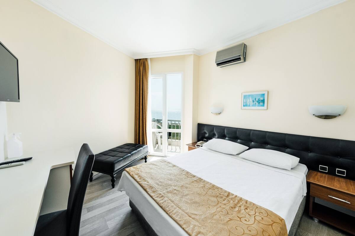 A hotel room with a bed, a desk, a chair, a TV, and a balcony with a view.