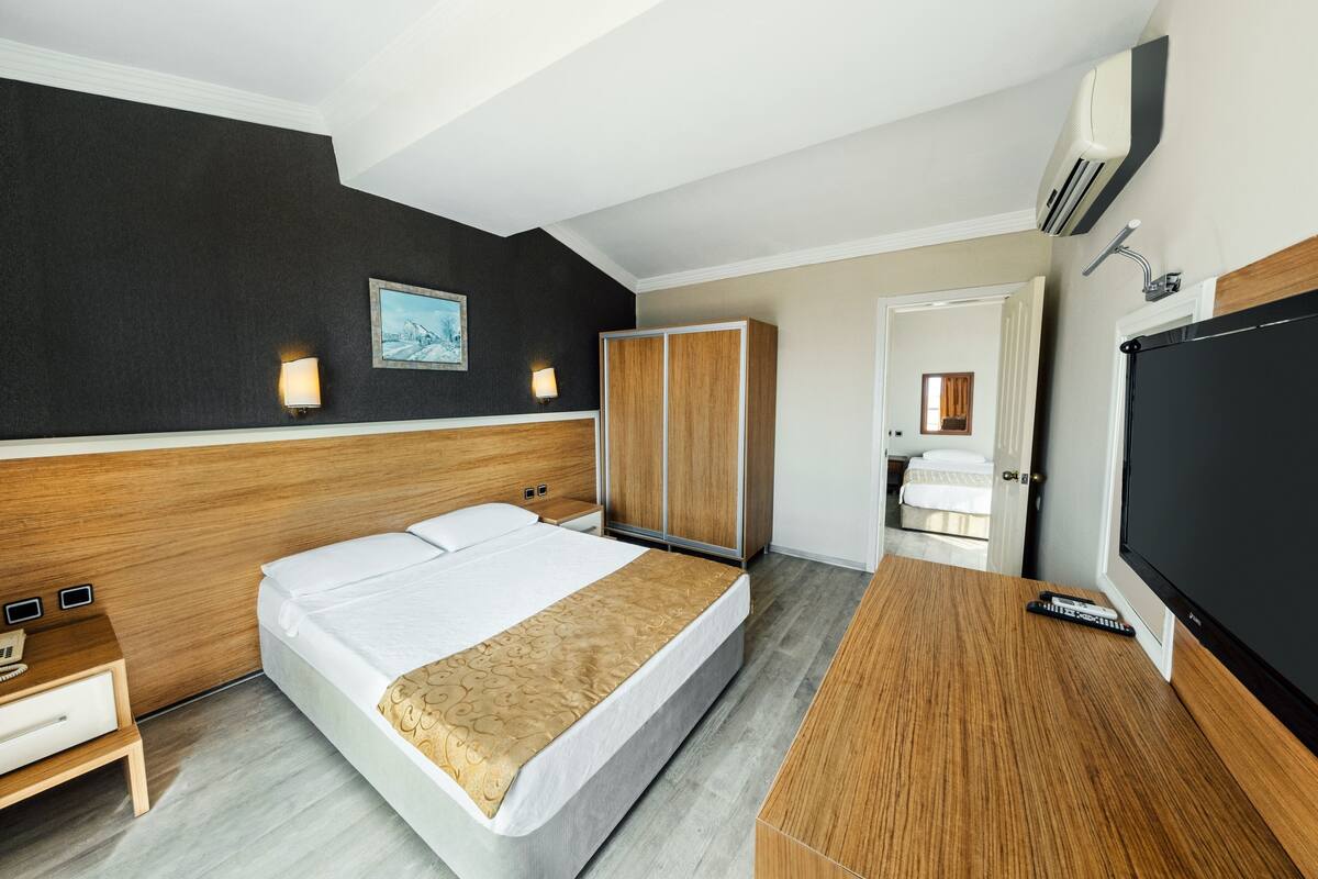 A hotel room with a bed, wooden wardrobe, bedside table, and a TV.