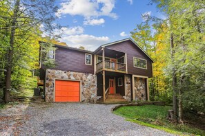 A two-story house with a stone facade, a red garage door, and a balcony. - Slopeside on Timberline Mountain's Salamander Trail-Perfect in every season! (Canaan Valley)
