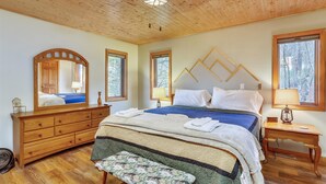 Een slaapkamer met een houten plafond, een bed met een blauwe deken, een houten dressoir en een bankje.