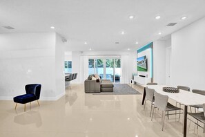 Un salon moderne doté d’une grande fenêtre, d’un coin repas avec une table blanche et d’une chaise bleue.