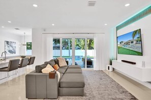 Un salon moderne comprenant un canapé d’angle, un coin repas et un téléviseur fixé au mur.
