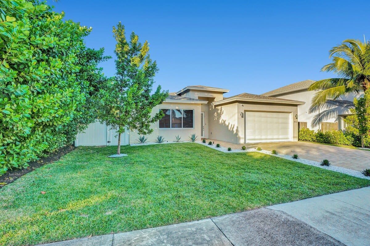 A modern house with a garage, a well-maintained lawn, and a palm tree.