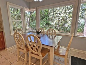 A dining area with a wooden table and chairs, large windows with a view of greenery, and a tiled floor. - Pet and Friendly Shipyard Home with 5 Beds/3.5 Baths Firepit and Private Pool (Hilton Head)