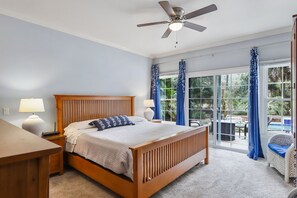 A bedroom with a wooden bed, two bedside lamps, a ceiling fan, and a view of a pool through large windows. - Pet and Friendly Shipyard Home with 5 Beds/3.5 Baths Firepit and Private Pool (Hilton Head)