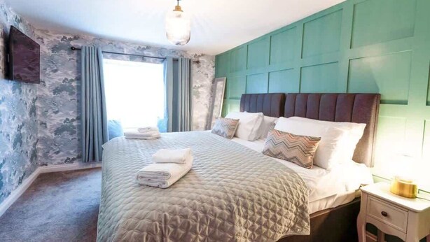A bedroom with a large bed, a bedside table, and a window with curtains.