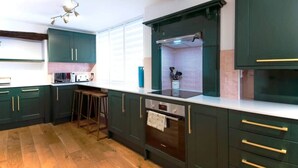 A kitchen with dark green cabinets, a white countertop, a built-in oven, and a bar stool.