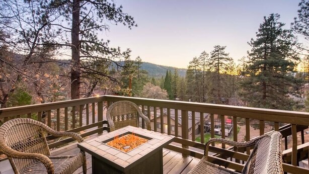 A deck with wicker chairs and a fire pit, overlooking a forested area. - Serene View Chalet | Hot Tub - King Beds Mtn Views (Big Bear Lake)
