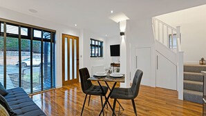 Un comedor moderno con suelo de madera, una mesa de comedor dispuesta con platos y vasos, y sillas negras.