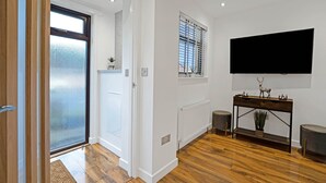 Una sala de estar moderna con piso de madera, un televisor de pantalla plana grande montado en la pared, una consola con objetos decorativos y un ventanal corredero que da a un espacio exterior.