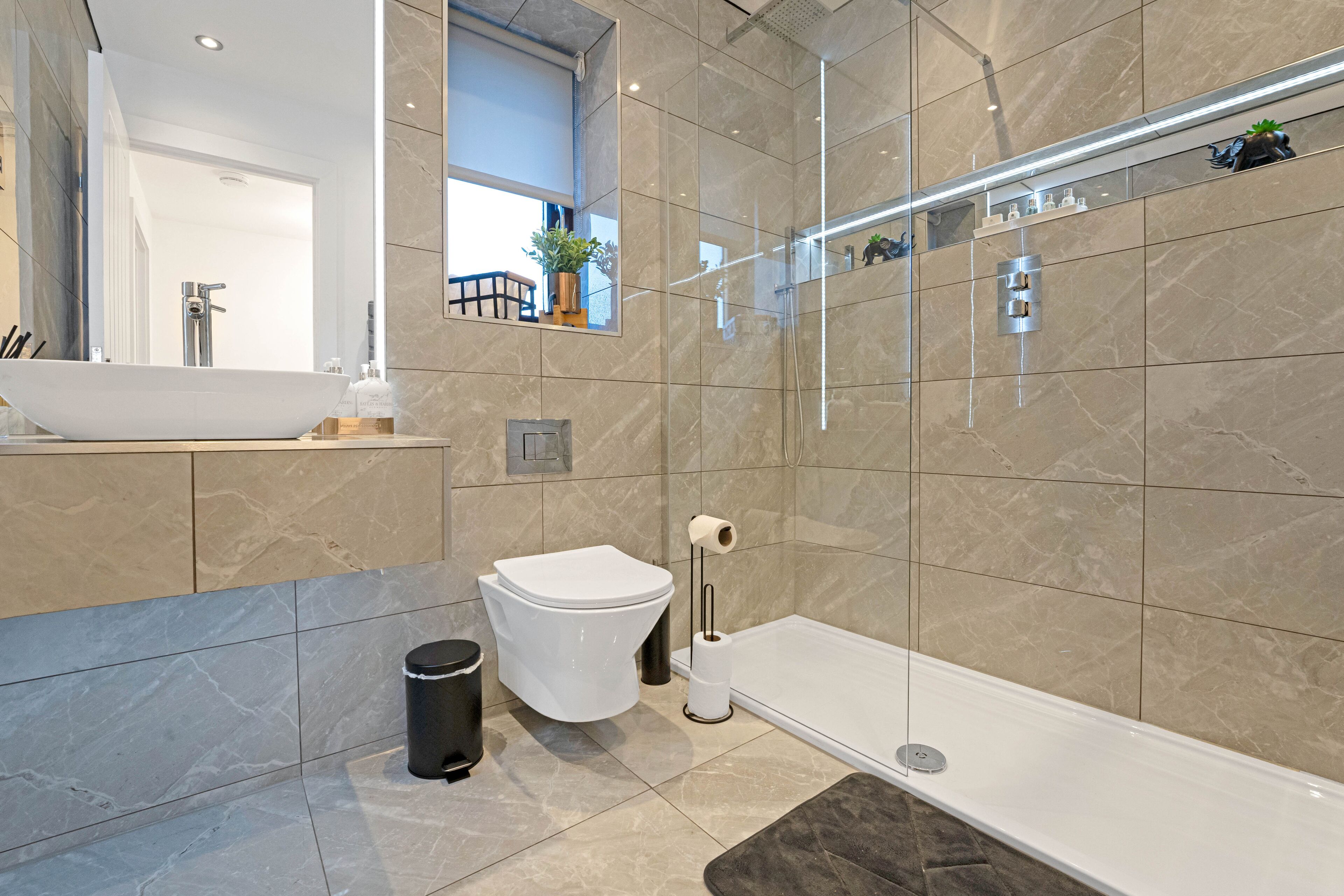 Une salle de bain moderne avec un grand miroir, un lavabo blanc, des toilettes et une douche à parois de verre.