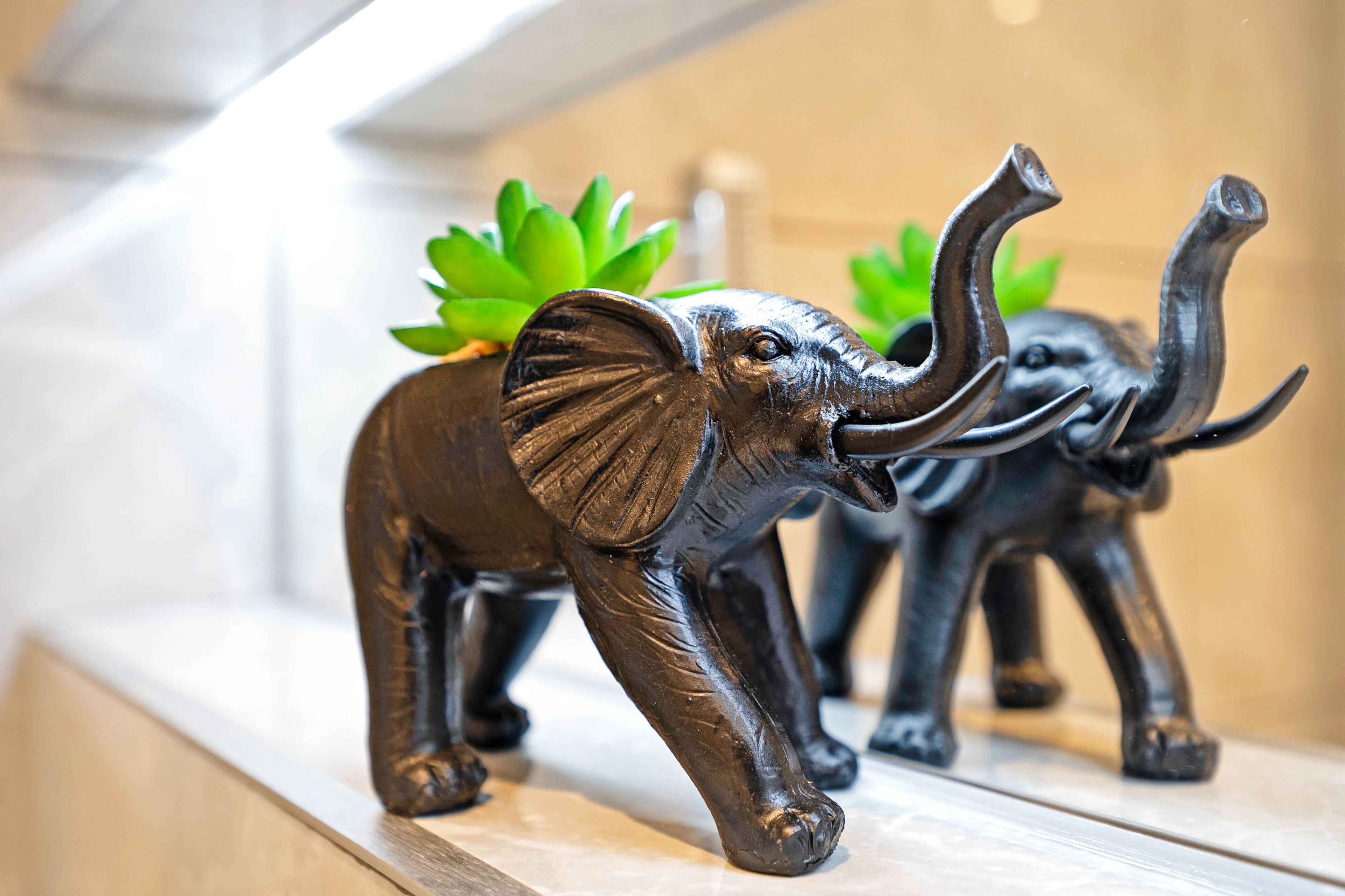 Une sculpture décorative représentant un éléphant, avec une plante verte sur son dos, placée sur une étagère.