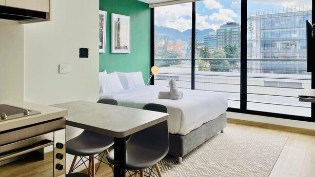 Une chambre d’hôtel moderne dotée d’une grande fenêtre, d’un lit, d’un coin repas et d’une kitchenette.