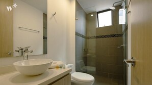 Een moderne badkamer met een grote witte wastafel, een toilet en een douchecabine met glazen wanden.