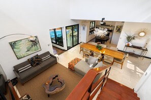 A spacious living area with a sofa, a coffee table, and a dining table. There is a staircase leading to an upper level.