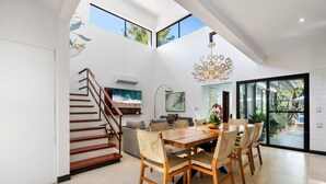 Un interior moderno con una mesa de comedor de madera, sillas, una escalera y ventanas amplias.